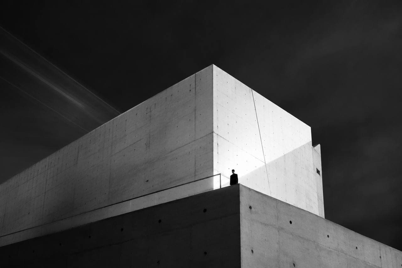 Concrete building with a lone figure on the roof under dramatic light